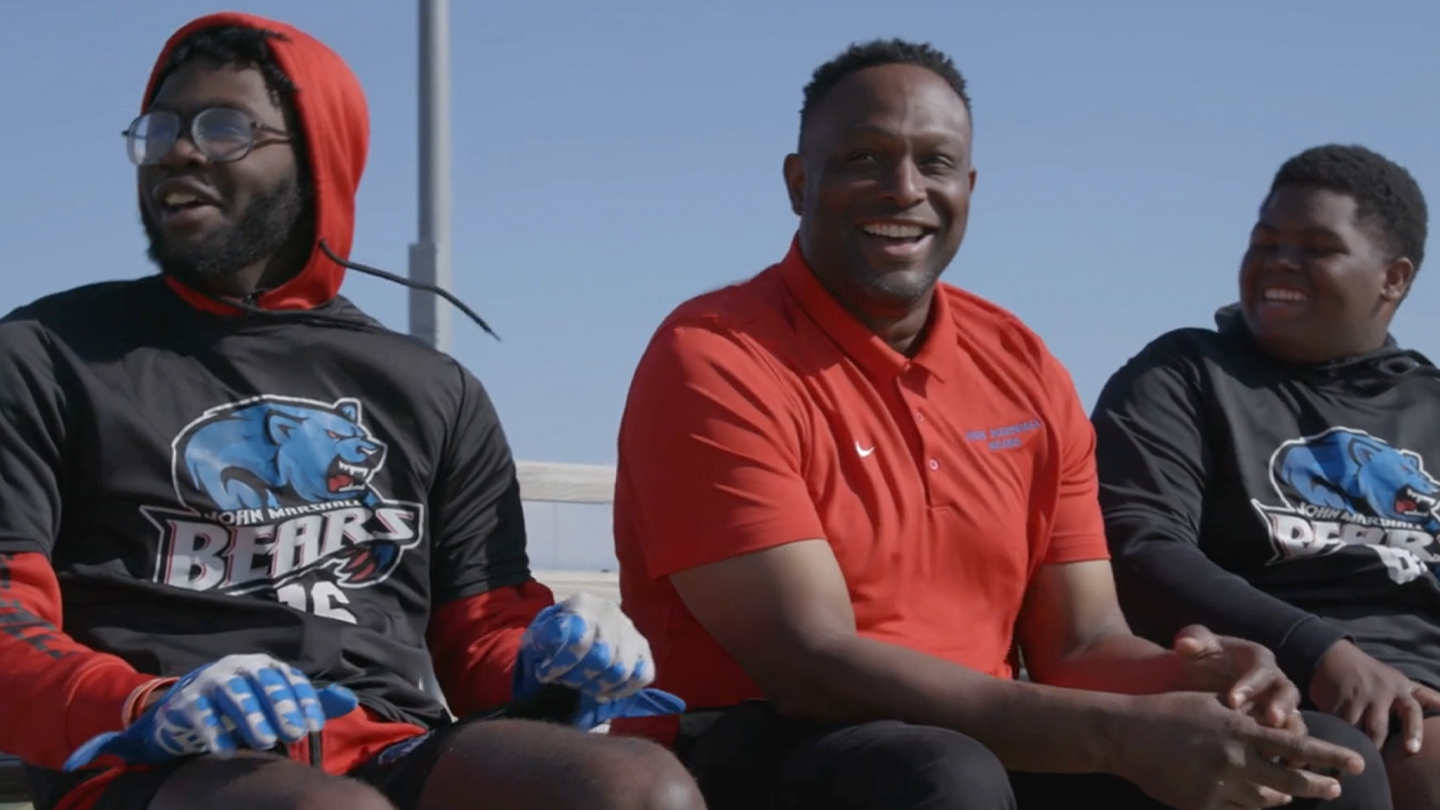 Coach Josh Norman sitting with student-athletes during the Coaching Against the Odds story on Power of Sports